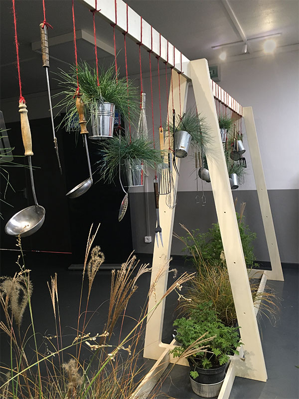 ustensiles de cuisine suspendus sur une structure en bois et garnis de plantes vertes