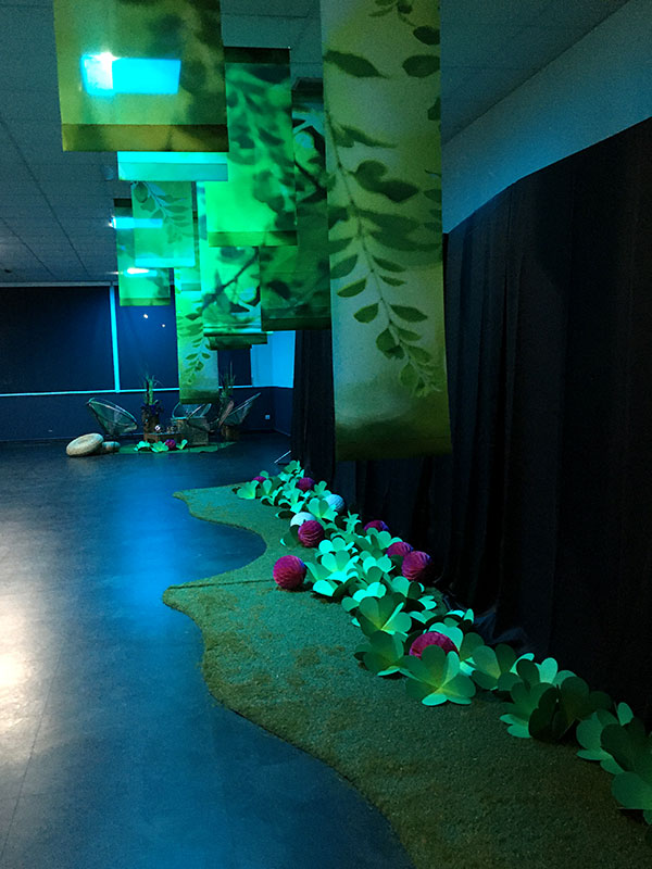 vue du vestiaire au sol des trefles en papier posés sur un chemin de moquette et faux gazon au plafond, succession de kakémonos au motif de feuillage